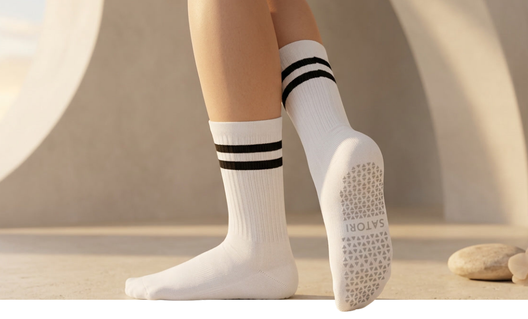 White Satori crew grip socks with black stripes on Pilates reformer, featuring non-slip sole for stability and balance.